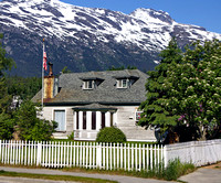 Cute house with white picket fence, flag and snow-capped mountains behind