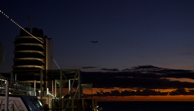 Sunset over Honolulu harbour with the ship's stack and an aircraft climbing out