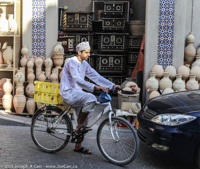 Young Omani man on a bicycle in front of a pot vendor