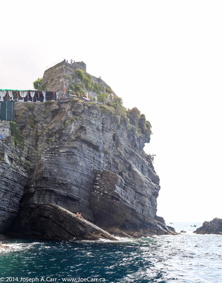 Sunbathers on a steep-sloped rock below a Vernazza cliff top resort