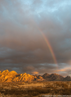 Sunset lighting the Dragoon Mountains with a rainbow in front of the storm clouds