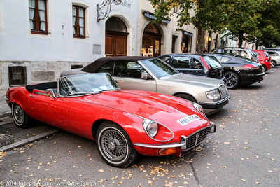High end cars parked in the street, including a classic Jaguar