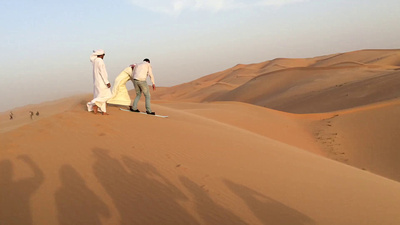 Our guide Kais rides a snowboard down a sand dune